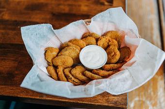 Product: A metal basket lined with white parchment paper, filled with crispy fried pickle fries and served with a small cup of ranch dressing on the side - RJ Grunts in Lincoln Park - Chicago, IL American Restaurants