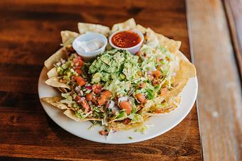 Product: a pile of nacho chips dopped with tomatoes, guacamole, chili, beans, and lettuce with a side of sauces. - RJ Grunts in Lincoln Park - Chicago, IL American Restaurants