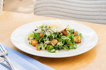 Product: A mixed green salad with cucumber, diced vegetables, croutons, and shredded cheese is served in a white bowl on a wooden table. - Summer House - Las Vegas in Las Vegas, NV Restaurants/Food & Dining