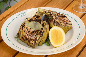 Product: Two grilled artichoke halves with char marks with a lemon on the side. Served on a white plate. - Summer House - Las Vegas in Las Vegas, NV Restaurants/Food & Dining