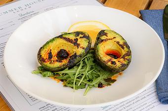 Product: Two grilled avocado halves with char marks sit on a bed of arugula, drizzled with salsa matcha, and garnished with an orange slice on a white plate. - Summer House - Las Vegas in Las Vegas, NV Restaurants/Food & Dining