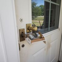 Uninstalled brass door lock replacement parts hanging on a white door by Peekskill Locksmith Co. Call Us (914) 867-4224