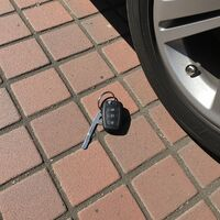 Car key fob with key blade lying on brick pavers next to a vehicle tire by Fishkill Secure Locksmith. Call Us (845) 773-1514