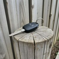 Car key fob with key blade resting on a wooden fence post by First Locksmiths. Call Us (845) 506-8280